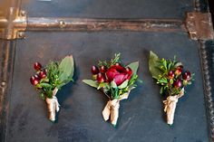 three boutonnieres with red flowers and greenery are on an old suitcase