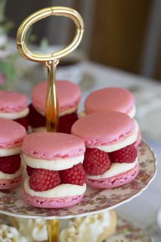 there are many pink and white macaroons on the cake plate with gold trim