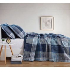 a bed with blue and white plaid bedspread on top of it next to a night stand