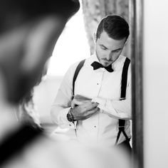 a man in a bow tie is looking at his watch while he adjusts his suspenders