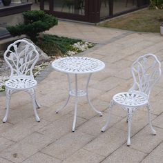 two white patio furniture sitting on top of a brick floor next to a garden table and chair