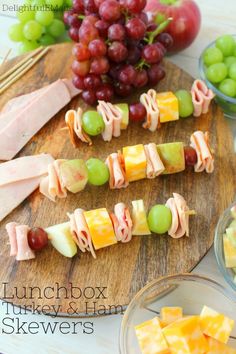 several different types of food are arranged on a cutting board with grapes, ham, and cheese