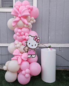 a bunch of balloons that are in the grass near a building with a hello kitty on it