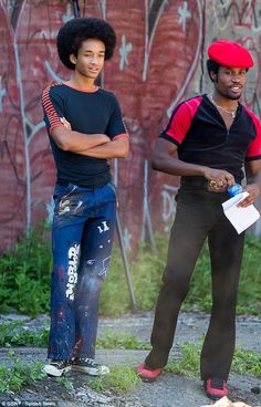 two young men standing next to each other in front of graffiti covered wall with arms crossed