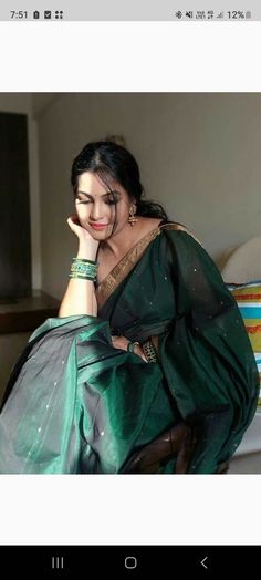 a woman sitting on top of a bed wearing a green sari and holding her hand to her face