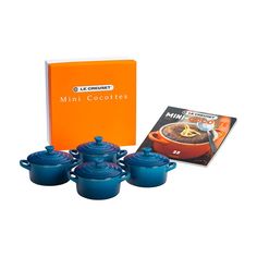 the mini cookware set is blue and has four pots on it, with an orange book behind it