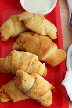 several pastries on a red plate next to a bowl of ranch dressing and dipping sauce