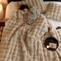 a woman laying in bed under a fluffy blanket