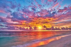 the sun is setting over the ocean with clouds in the sky and sand on the beach