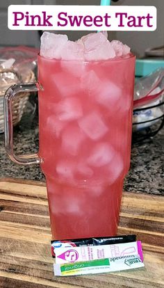 a pink sweet tart drink with ice in it on a wooden table next to a candy bar