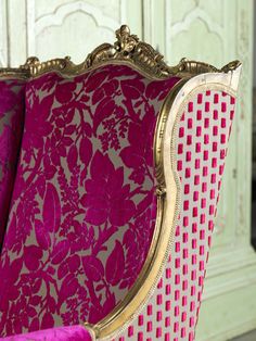 an ornately decorated chair with pink and gold fabric on the back, sitting in front of a green cabinet