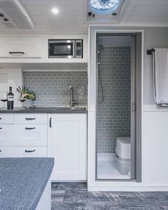 a kitchen with white cabinets and gray counter tops, along with an open door leading to the bathroom