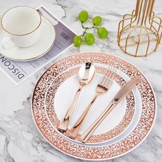 two forks and one knife on a plate next to a cup, saucer and book