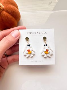 a pair of white and yellow earrings with an orange bird on the front, sitting next to a pumpkin