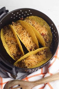 three tacos in a colander with shredded cheese on top