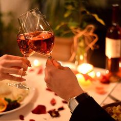 two people are toasting with wine at a dinner table filled with food and candles