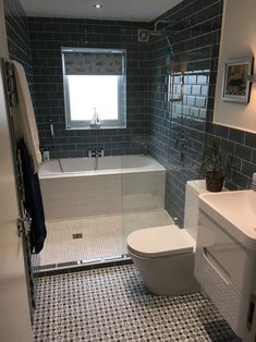 a white toilet sitting next to a bath tub in a bathroom with blue tiles on the walls