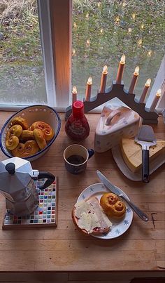 a wooden table topped with lots of food next to a window filled with lit candles