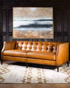 a brown leather couch sitting in front of a painting