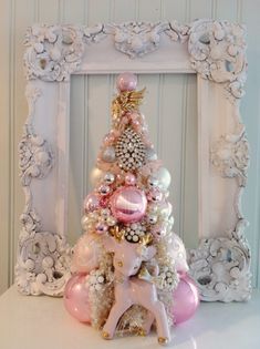 a small christmas tree with pink and white ornaments in front of an ornate framed frame