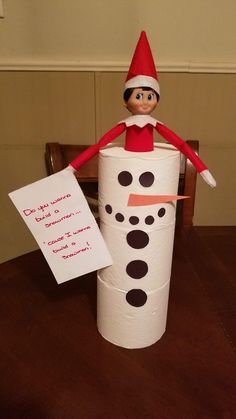 an elf is sitting on top of a toilet paper roll with a note attached to it