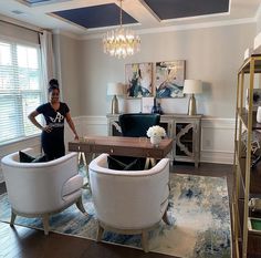 a woman standing in a living room next to two white chairs and a coffee table