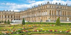 an elaborate garden in front of a large building with hedges and flowers on the ground