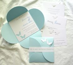 the wedding stationery is laid out on top of the bed with white sheets and blue paper