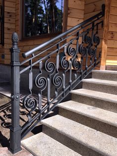 an iron hand rail on a stair case in front of a wooden house with stone steps