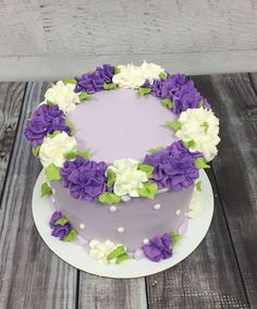 a cake with purple and white flowers on it sitting on a wooden table next to a wall