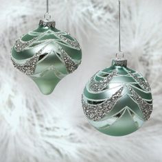 two ornaments are hanging on a white furnishing background, one is green and the other is silver