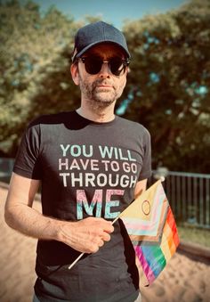 a man holding a rainbow kite in his right hand and wearing a t - shirt that says you will have to go through me