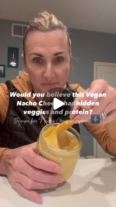 a woman holding a jar filled with food and looking at the camera while sitting at a table