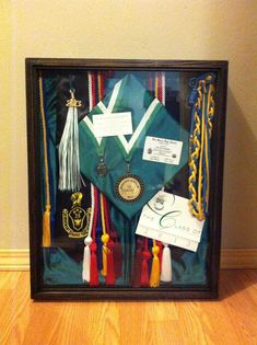 a graduation cap, gown and other items are in a shadow box on the floor