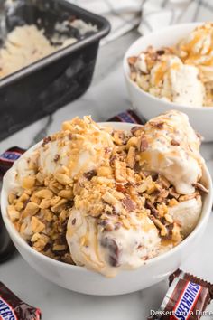 two bowls filled with ice cream covered in nuts and caramels next to chocolate bars