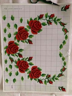 a cross stitch pattern with red roses and green leaves on white paper next to scissors