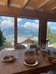 a table with plates of food on it in front of a large window overlooking the mountains