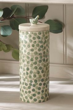 a white and green canister sitting on top of a table next to a plant