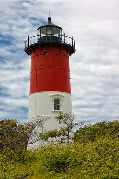 a red and white light house sitting on top of a lush green hillside under a cloudy blue sky