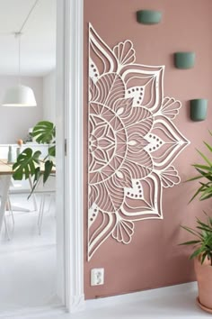 an intricately designed wall hanging on the side of a pink wall with potted plants