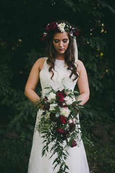 a woman wearing a wedding dress holding a bouquet of flowers and greenery in her hands