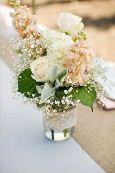 a vase filled with white and pink flowers sitting on top of a blue table cloth