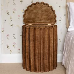 a wicker storage basket sitting on top of a bed next to a wallpapered wall