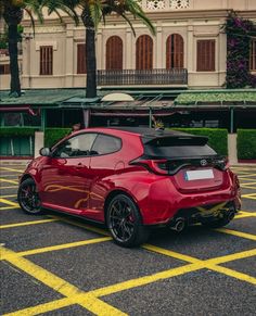 a red sports car parked in a parking lot next to a building with palm trees