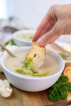 a person dipping something into a bowl of broccoli soup with bread on the side