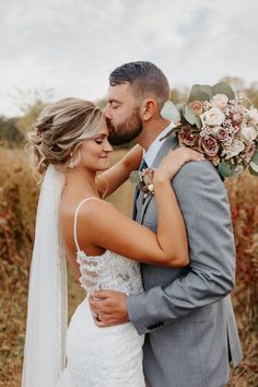 a bride and groom embracing each other in front of tall grass