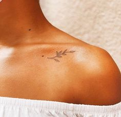 the back of a woman's shoulder with a small branch tattoo on her left shoulder