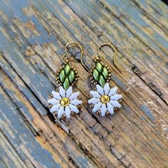 two white flowers with green leaves on them sitting on a wooden surface next to a pair of gold earwires