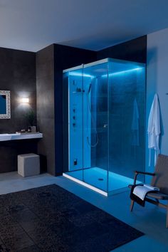 a modern bathroom with blue lighting on the shower wall and black walls, along with a white chair