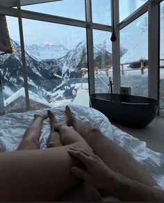 a person laying on top of a bed in front of a window with snow covered mountains